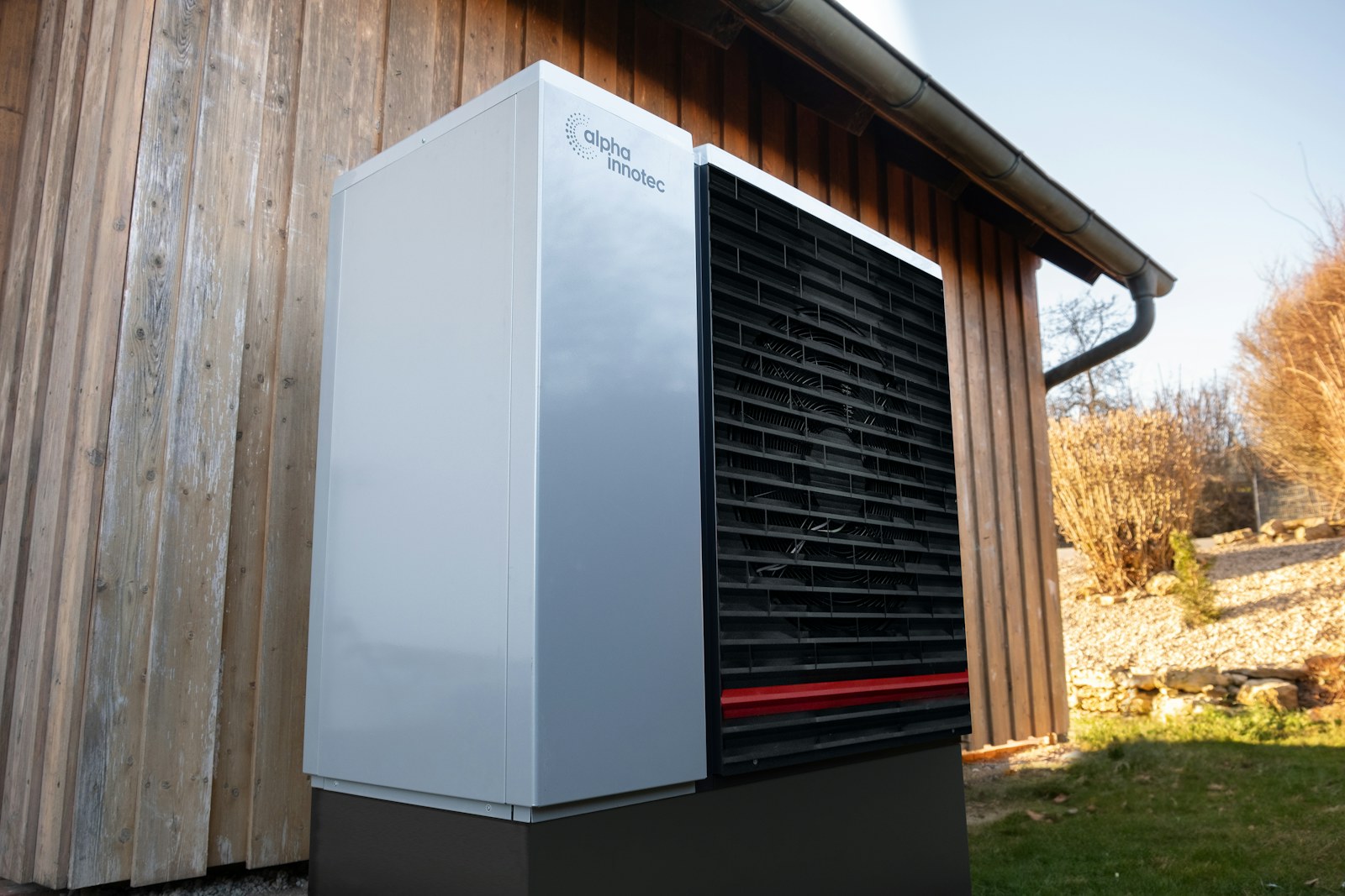 A white and black outdoor heat-pump unit mounted beside a building
