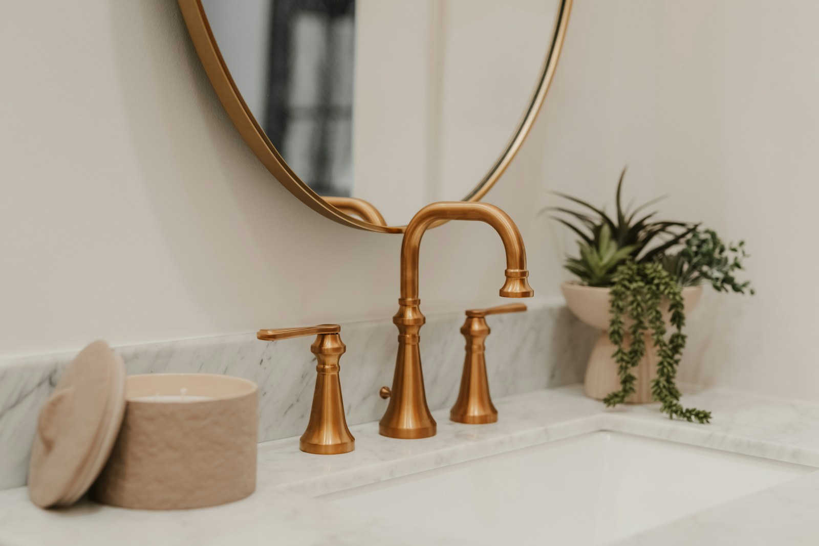 A modern brass bathroom faucet beside a small potted plant