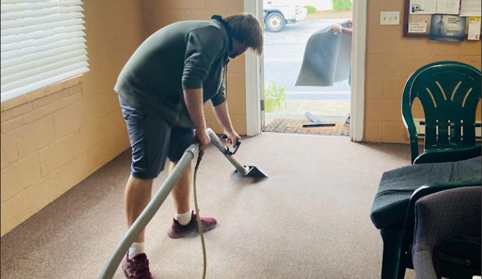 A technician guiding an extraction wand over carpet inside a home